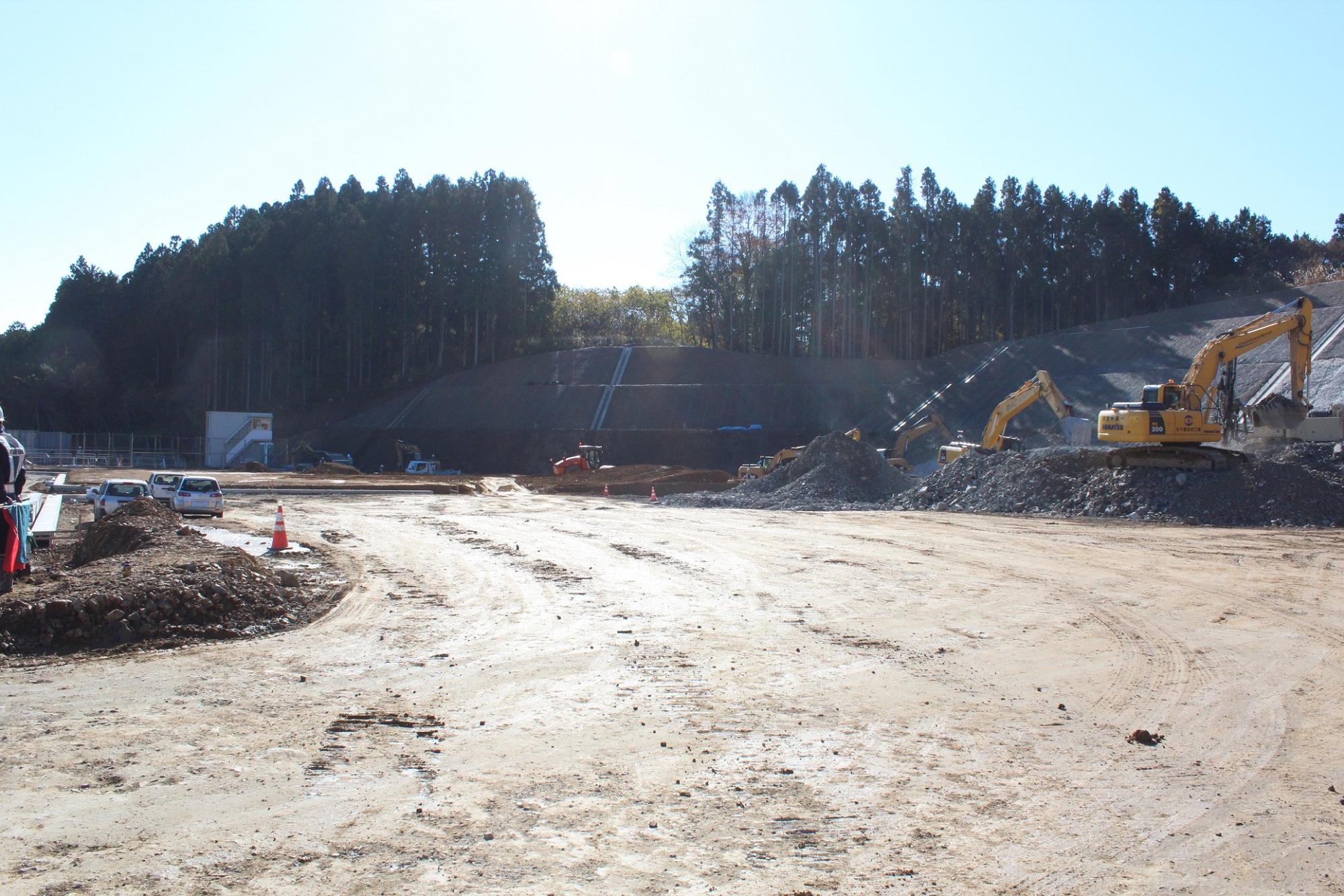 山林を背にした斜面の造成工事現場で、重機が土砂を運んでいる様子の写真