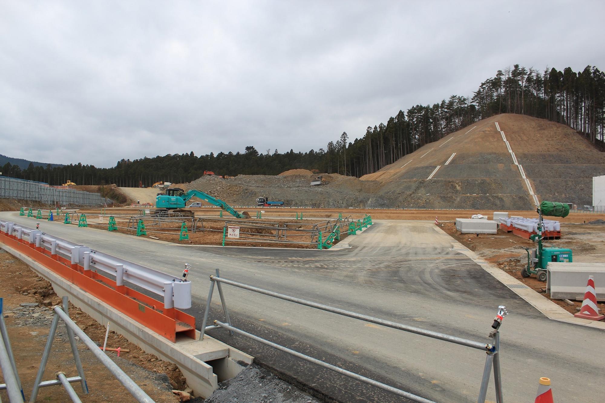 整備が進んだ造成地にアスファルト道路と法面が見える工事現場の写真