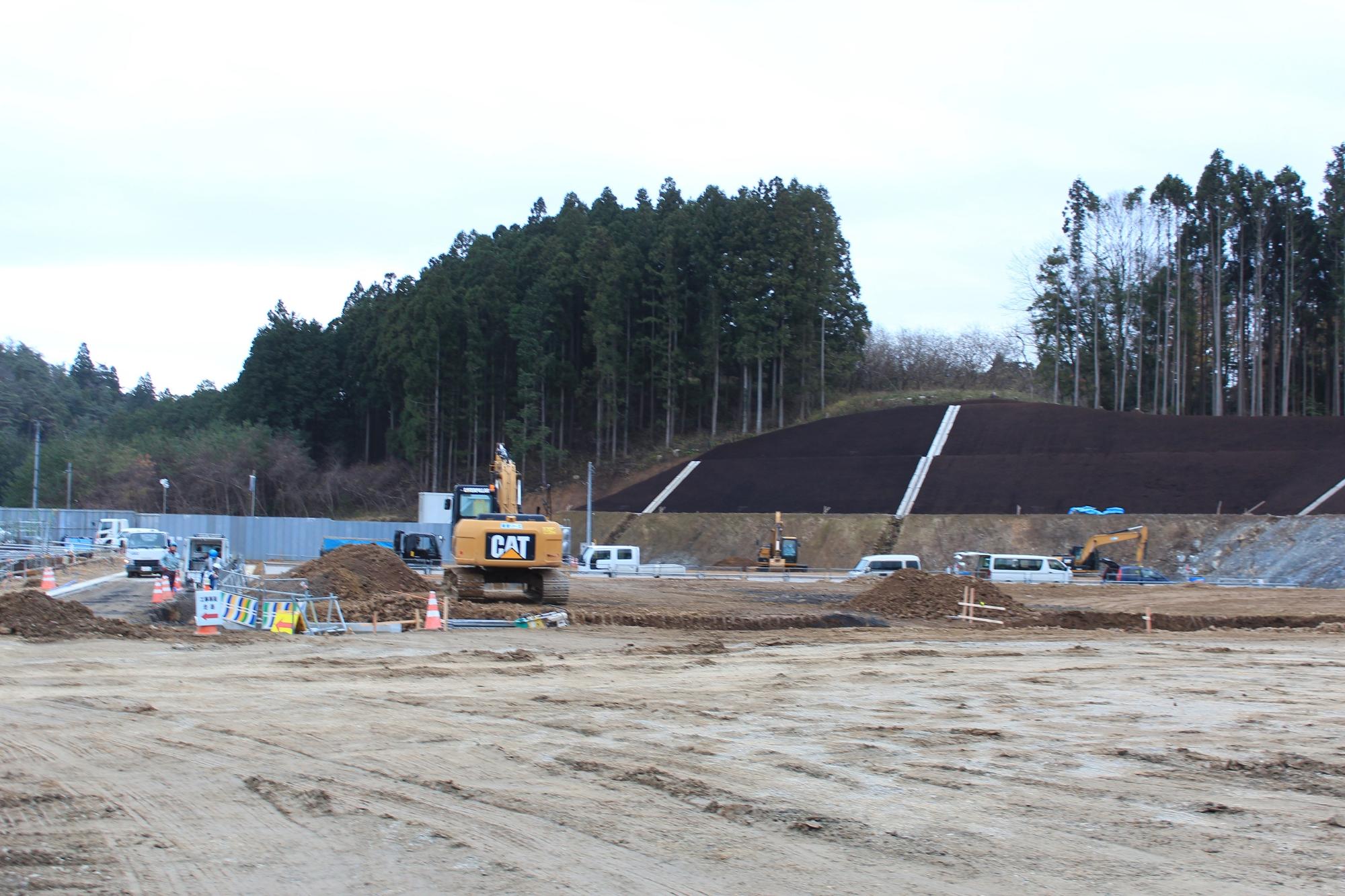 法面整備が進んだ造成地で複数の工事車両が作業している様子の写真