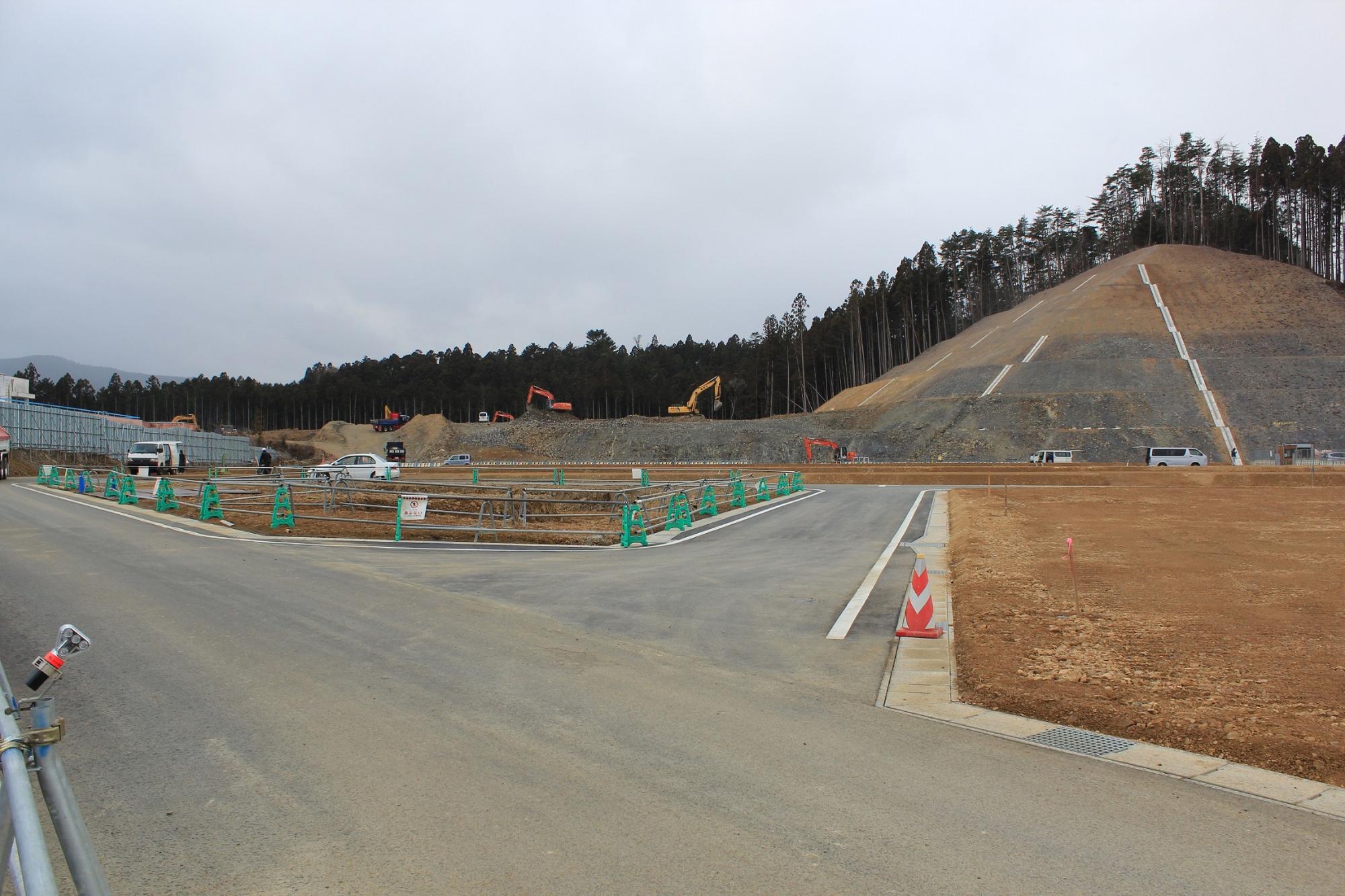 交差点状に舗装された道路と山裾の法面が見える造成地の写真