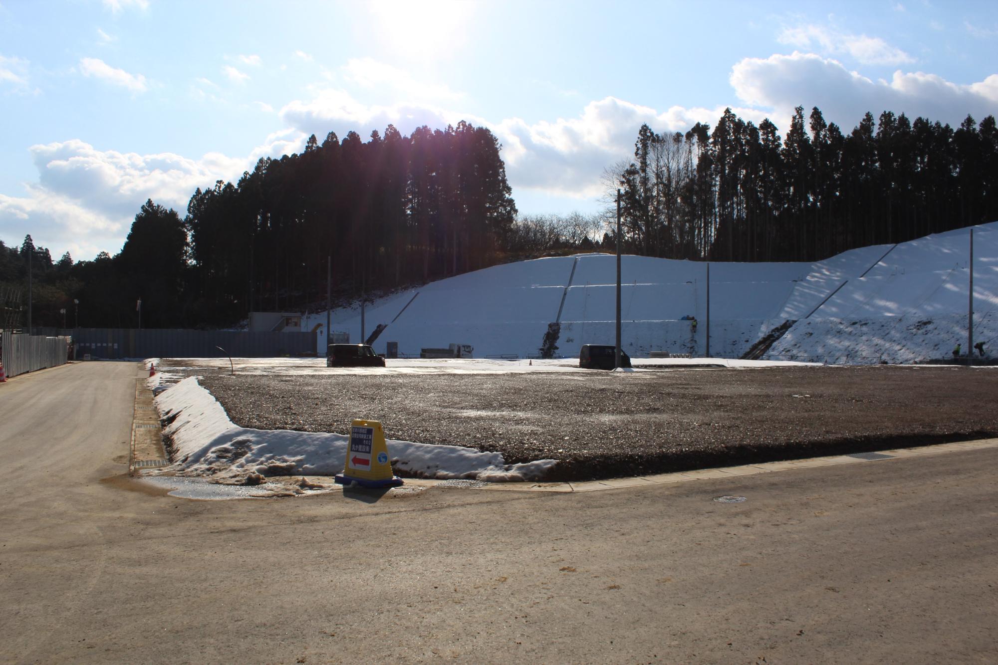 雪が積もった法面と舗装された道が見える冬の造成地の写真