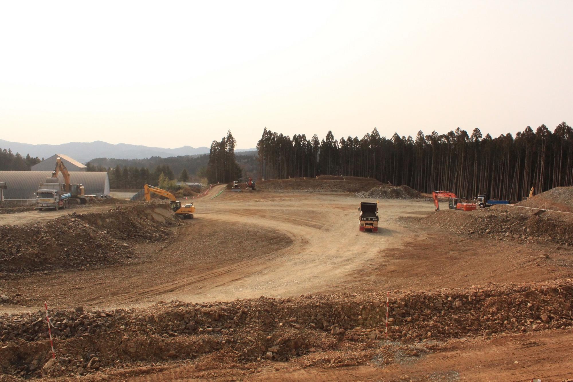 カーブした造成道路の両脇で重機が土を運んでいる造成地の写真