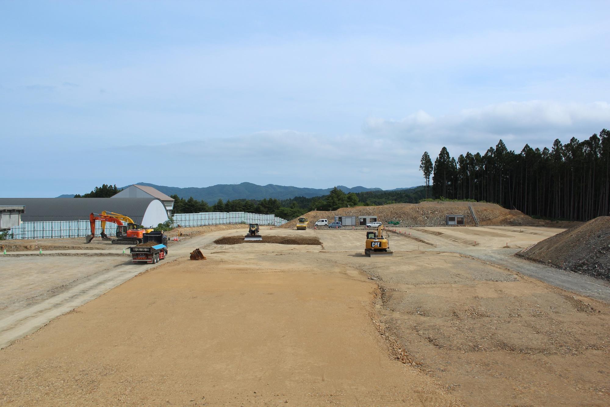 地面の整地が進み重機やダンプカーが複数稼働している工事中の様子の写真
