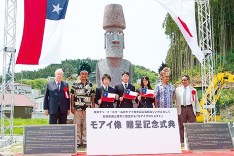 モアイ像をバックにチリの国旗旗を持った学生3名と関係者の方々が4名並んで写っているモアイ像贈呈記念式典の写真