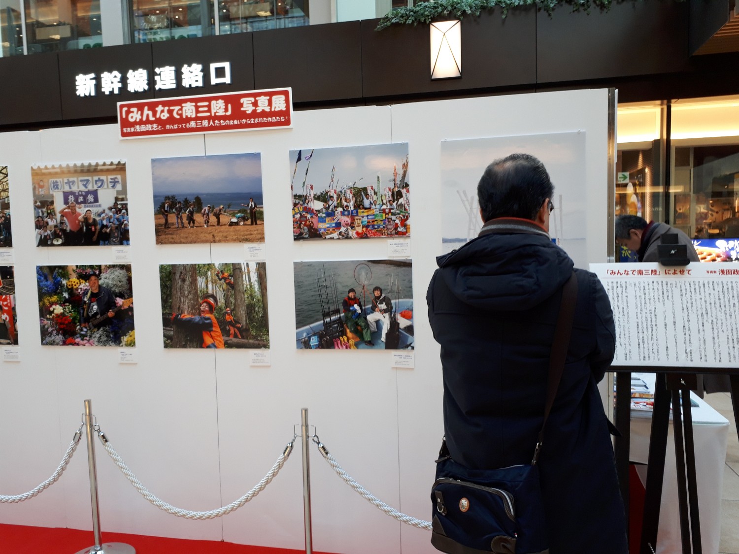 南三陸町の復興をテーマにした写真展の展示パネルを、黒いジャケットを着た中年男性が熱心に見入っている様子の写真