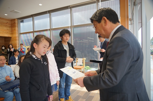 市長と女の子が向かい合って立ち、市長が手に持った感謝状を読み上げている様子の写真