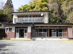 広い窓と二階に長いベランダ、白い外壁に下部が赤茶色のタイル調になっている二階建て住宅の写真