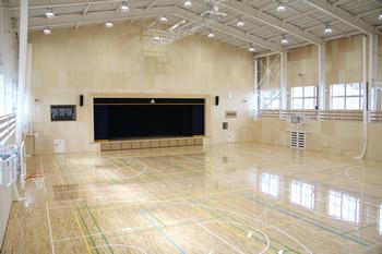 三角屋根で高い天井、床にはバスケットコートなど様々な競技のラインが引かれ、窓から明かりが差し込んでいる真新しい体育館全体を写した写真