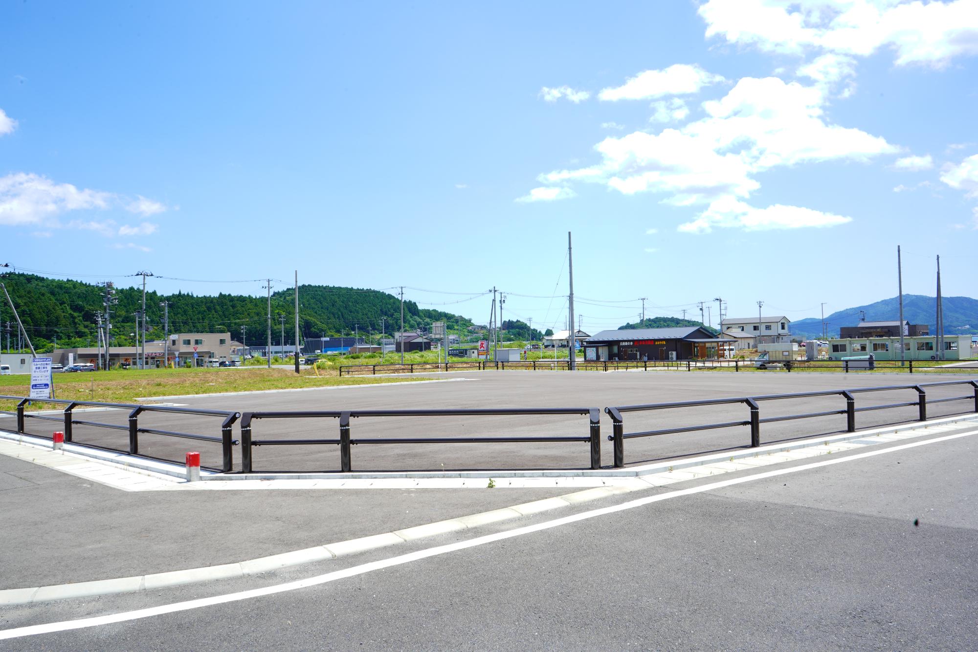 柵で囲まれた舗装された広場があり、奥に複数の建物が見えるうみべの広場（A）の写真