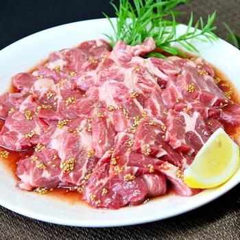 白いお皿の上に、生の薄切り肉が並べられ、肉にはソースとゴマのような小さな粒が散らされている写真