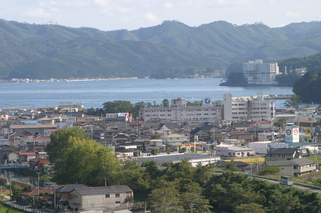 遠くに山並みが見え、海を挟んで手前には町並みが広がっている様子を写した写真