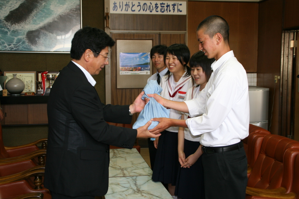 町長が、男女3人の生徒から水色の袋に入った義援金を笑顔で受け取っている様子写真