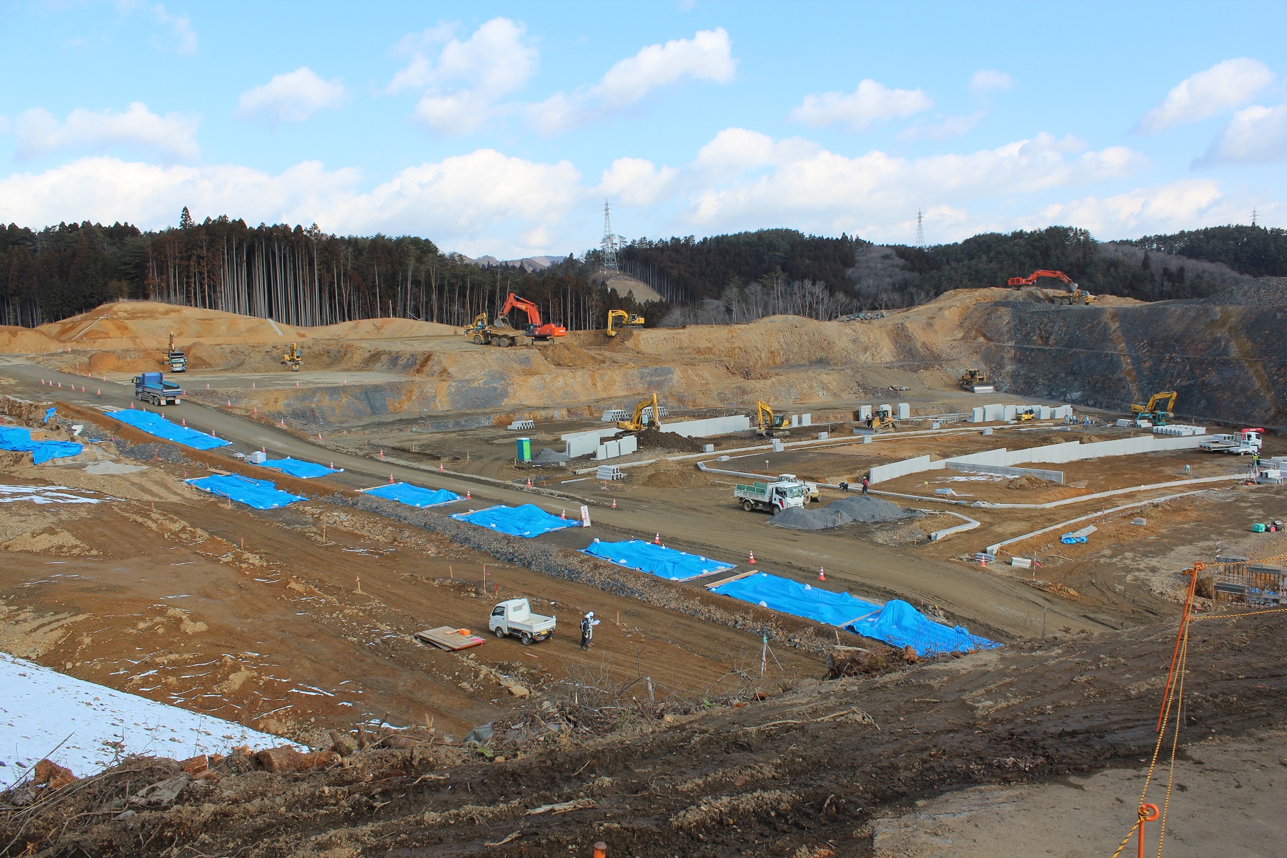整備が進んだ造成地にブルーシートで覆われた何箇所かの更地や資材置き場が見える写真