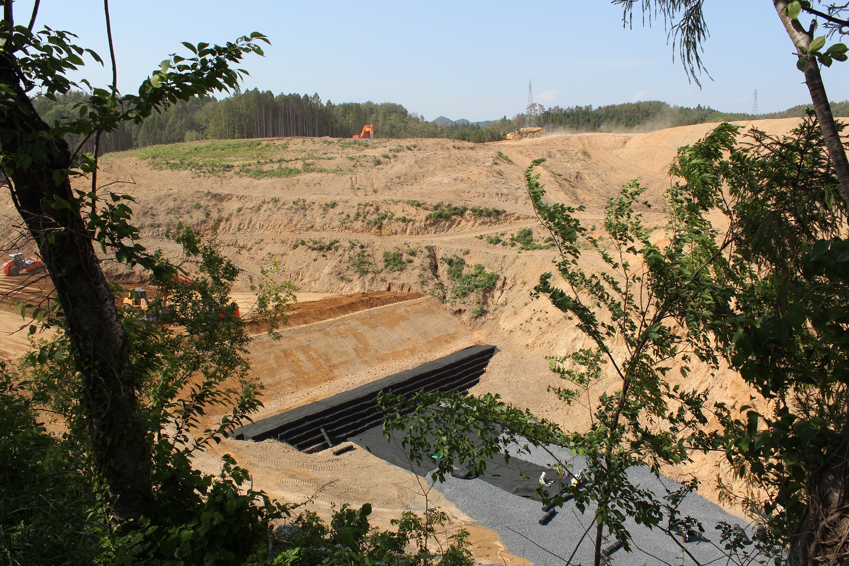 増税地の手前に擁壁のような物が造られ、奥の高い位置ではショベルカーやダンプカーが稼働している様子の写真