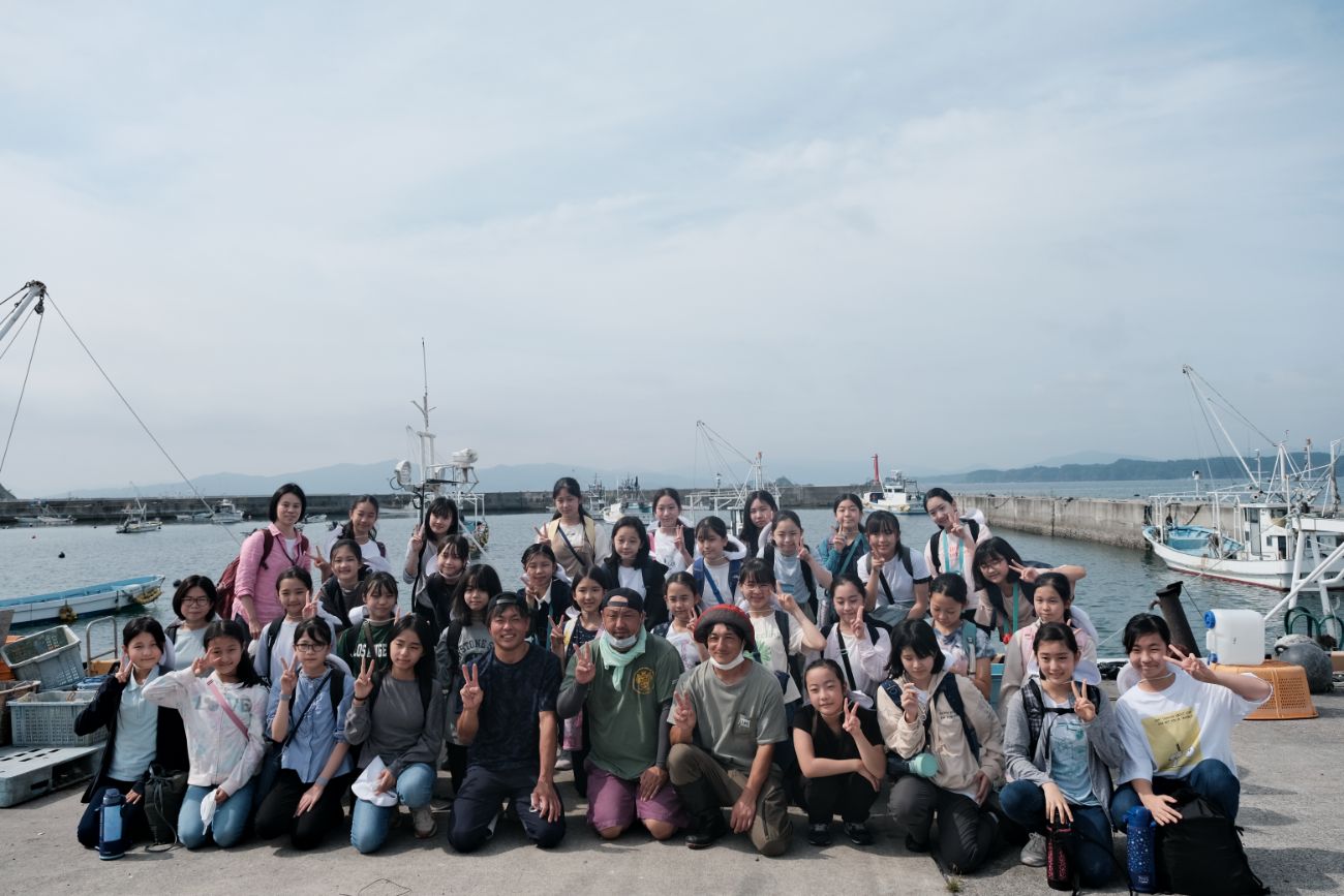 海辺の港で大勢の活動に参加した子どもたちと数名の大人が集合写真