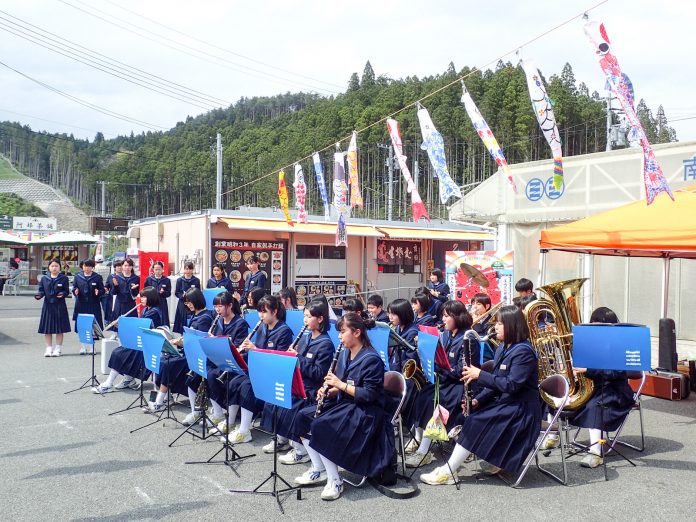 こいのぼりが空に泳ぐ中、制服姿の吹奏楽部の生徒たちが南三陸さんさん商店街の一角で楽器を演奏している写真