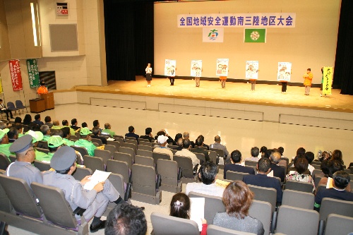 「全国地域安全運動 南三陸地区大会」の横断幕が掲げられたホールで、大勢の参加者が着席し、ステージ上で啓発パネルを持った人々が発表をしている集会の様子の写真