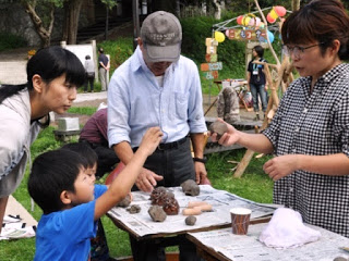 屋外のテーブルの上に粘土細工の材料が並べられ、大人と子どもが楽しそうに作品を作っている写真