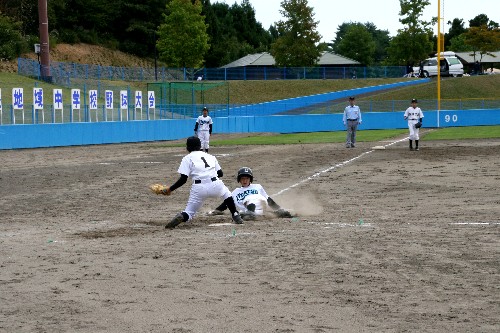 ユニフォームを着た選手が、野球の試合中に土煙を上げながら三塁へ果敢にスライディングをしている瞬間を捉えた写真