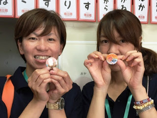 二人の女性が笑顔で手作りのバッジを手に持ち、カメラに向かって見せている写真