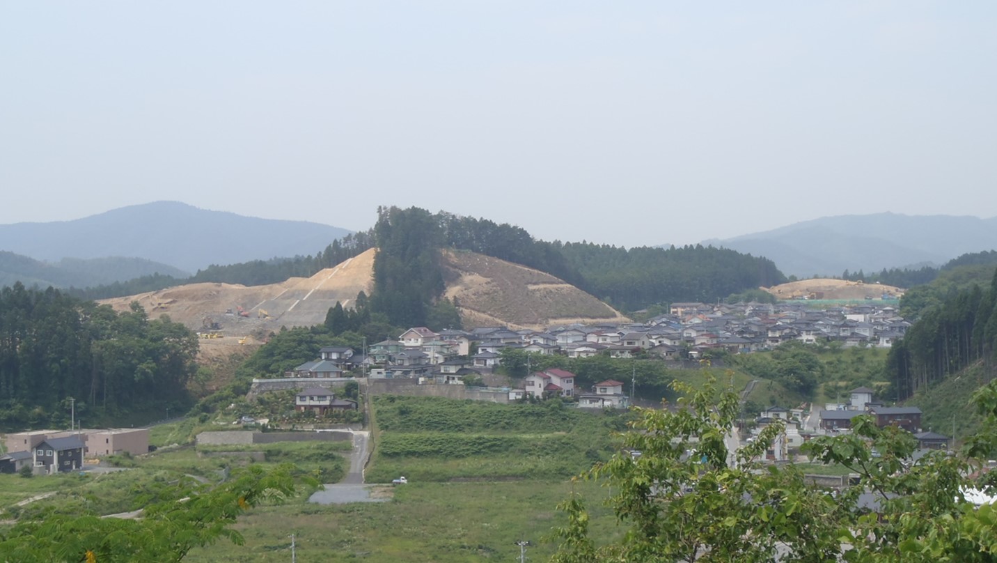 小高い山を切り崩して宅地造成が進められている遠景の町並みと造成地の写真