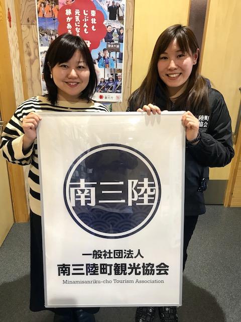 女性リポーターと黒いジャンパーを着た千葉さんが並び、南三陸町観光協会のロゴが大きく印刷されたパネルを持って笑顔を見せている写真