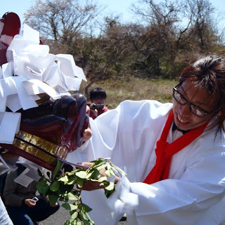 白装束姿の男性が、紙垂を頭に乗せた獅子舞の口に榊を銜えさせている様子の写真