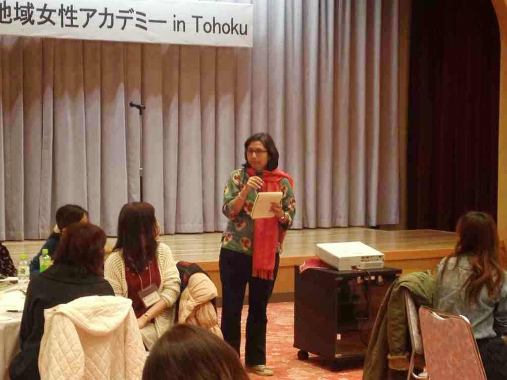 舞台の前で女性がマイクを片手に参加者にむけて話をしている写真