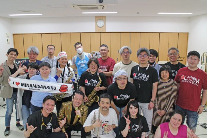 屋内の練習室で、楽器やマイクを持ったバンドメンバーが並んでいる集合写真