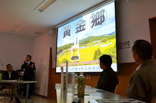 「黄金郷」と大きく書かれた農村風景のスライドを映しながら、前で男性が説明し、他の参加者が聞いている写真