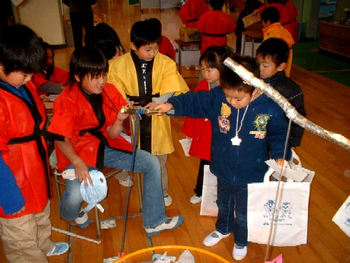 赤や黄色の法被を着た子どもたちが、手作りのお祭り道具を使って遊んでいる様子の写真