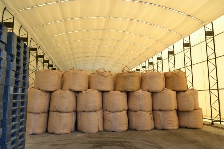 クリーム色の屋根の倉庫内に、茶色の巨大な袋が3段に積まれて整然と並んでいる写真