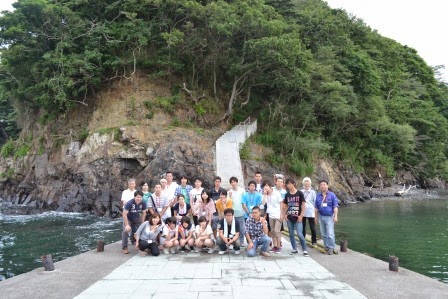 緑に覆われた小さな島のような丘の前にある桟橋に、二十数名の若者たちが並んでいる集合写真