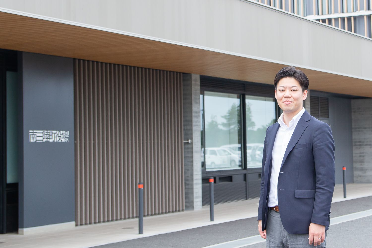 「南三陸町役場」と書かれた現代的な建物の前にスーツ姿の男性が立っている写真