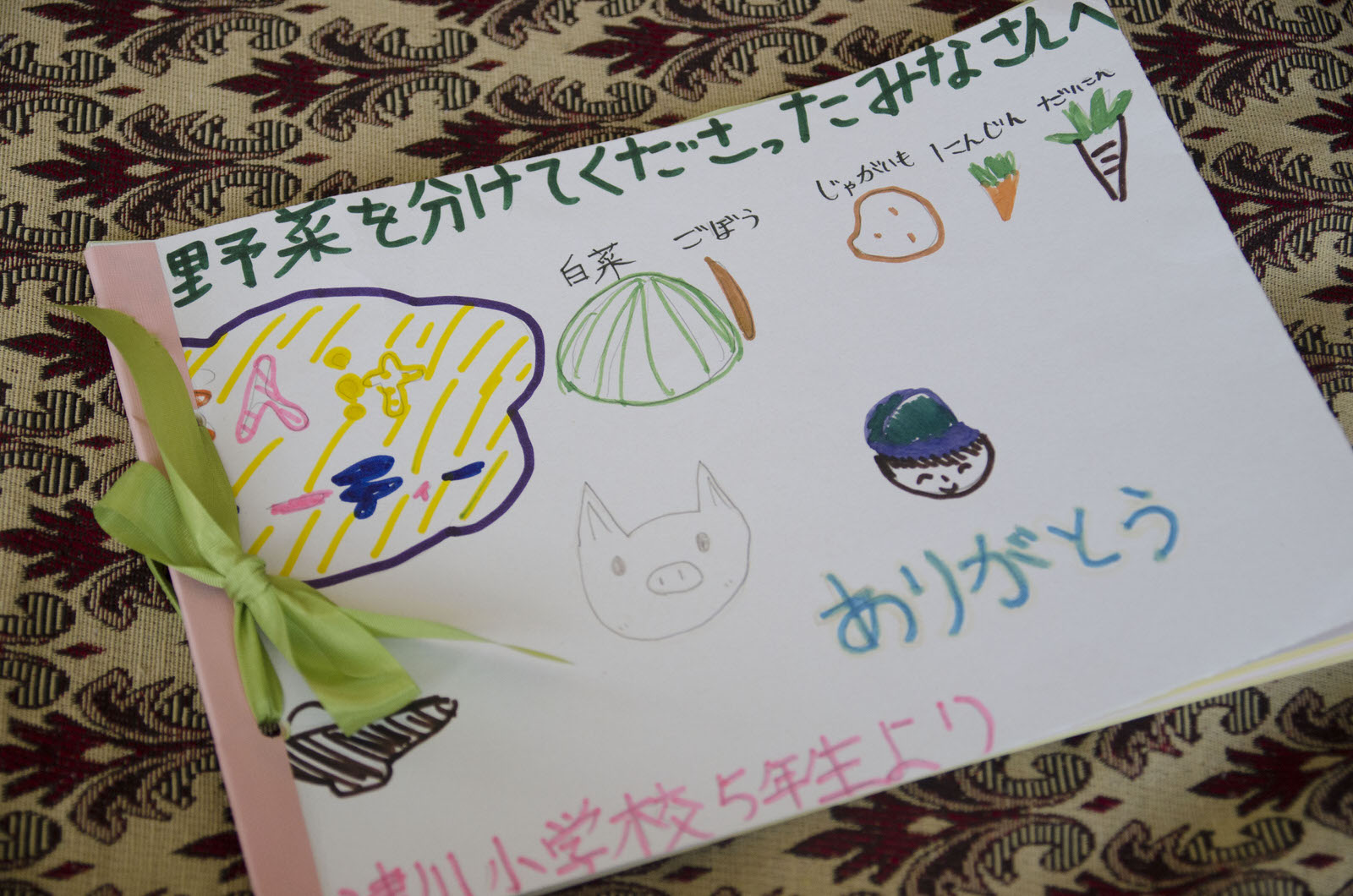 色鉛筆で野菜や動物、顔などが描かれた表紙に、「野菜を分けてくださったみなさんへ」と書かれた児童たちの感謝の気持ちが書かれている写真