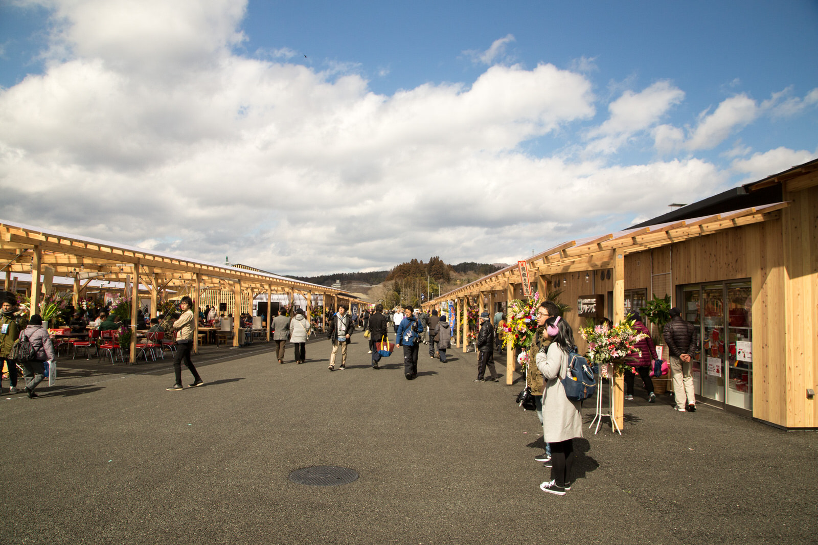 新しく建てられた木造の店舗が立ち並ぶ通りを多くの人が歩いていて、道の両側には飲食店やお店が並び、花束や開店祝いの装飾が施されている、オープン初日の商店街の様子の写真