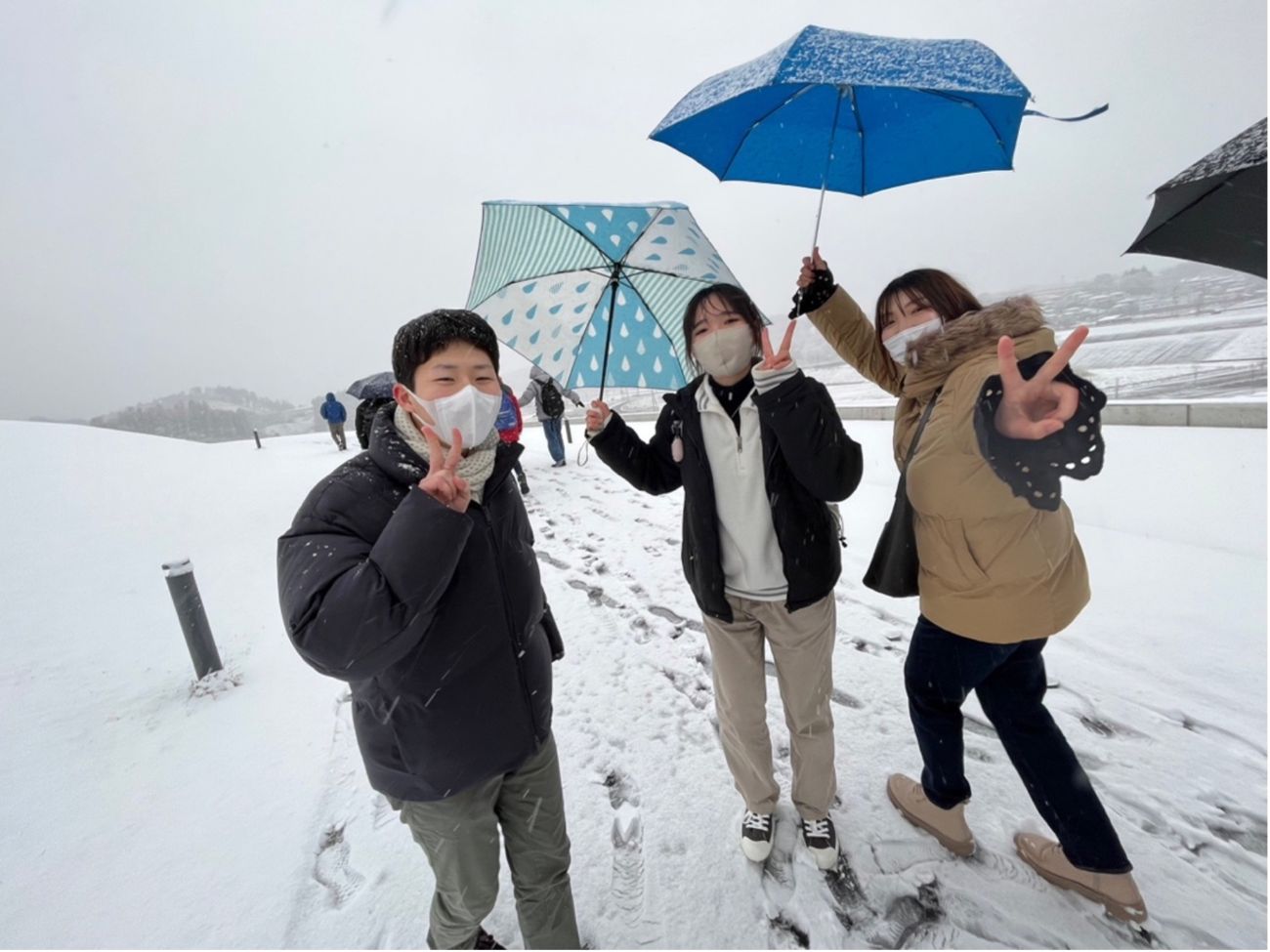 雪の中で傘を差した若者たちが楽しそうにポーズをとっている様子の写真