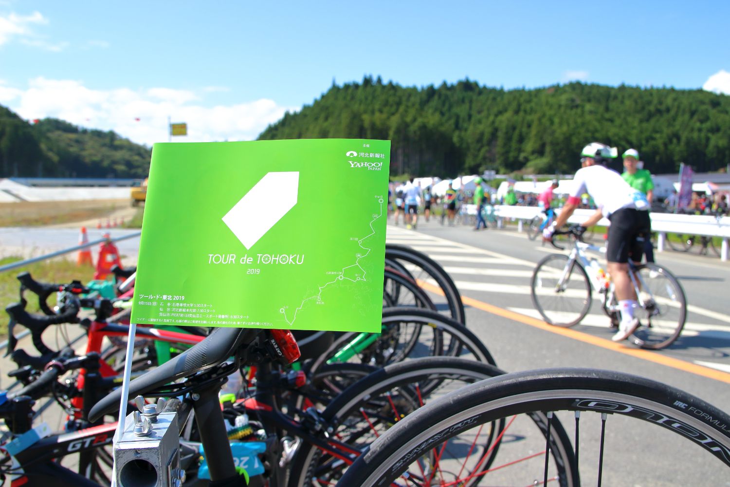 一列に並んで停まっている手前の自転車に英語で「TOUR de TOHOKU」と書かれた黄緑色の旗が設置された写真
