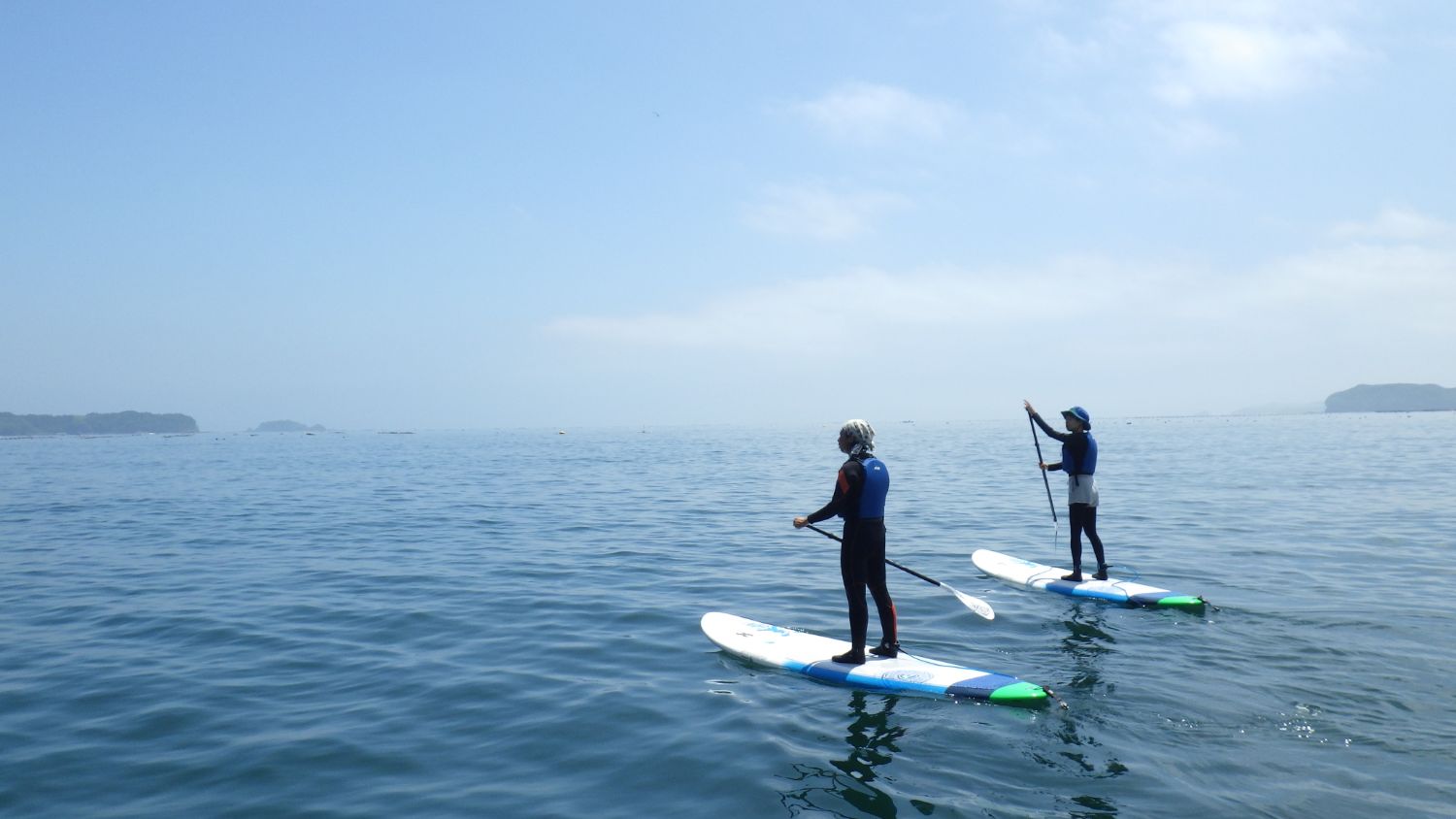穏やかな海の上で、二人の人がスタンドアップパドルボードを楽しんでいる様子の写真