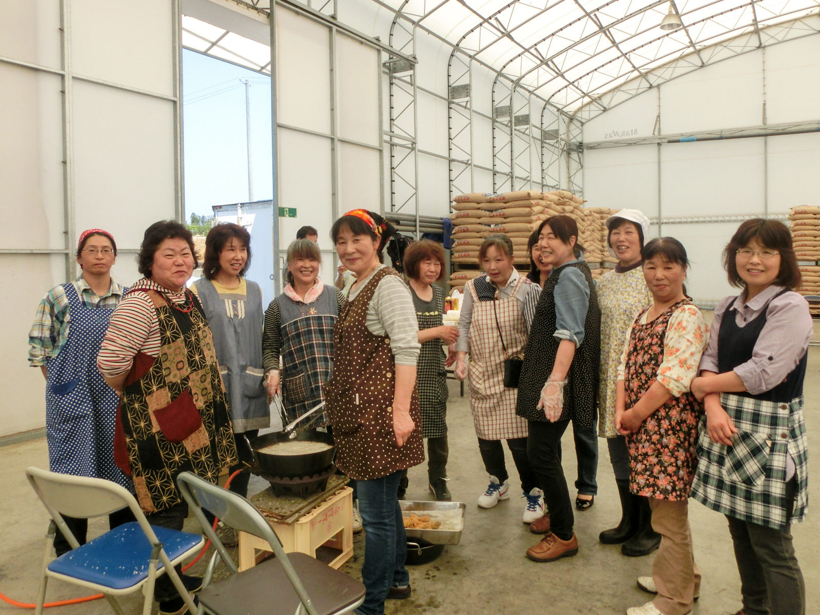 大きなテントの中で、たくさんのエプロン姿の女性たちが鍋の前に集まり笑顔でカメラを見ている写真