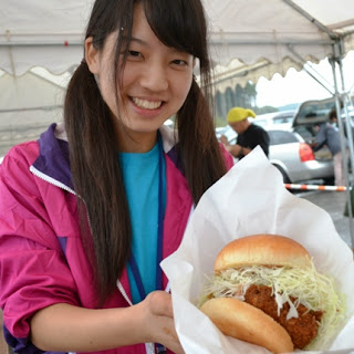 女性が大きな白い紙に包まれた千切りキャベツ入りの揚げ物バーガーを両手で持って見せている写真