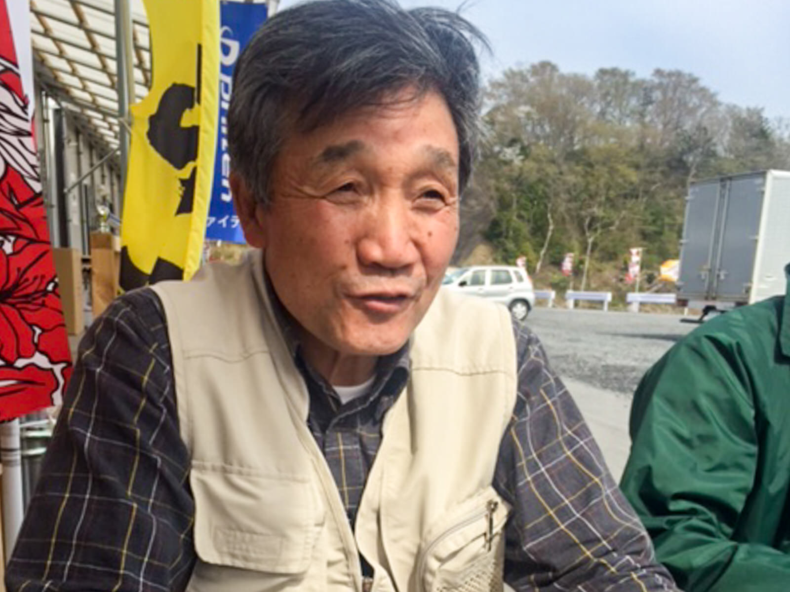 商店街ののぼりを背景に笑顔で話をしている小野寺さんの写真