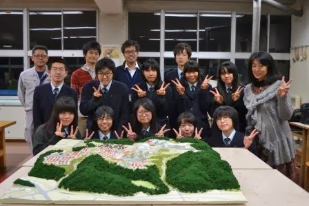 完成した立体模型の前で高校生と関係者の方々が笑顔でピースサインをしながら写っている集合写真