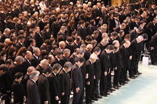 黒い礼服を着た参加者の方々が頭を下げて黙とうしている様子を写した写真