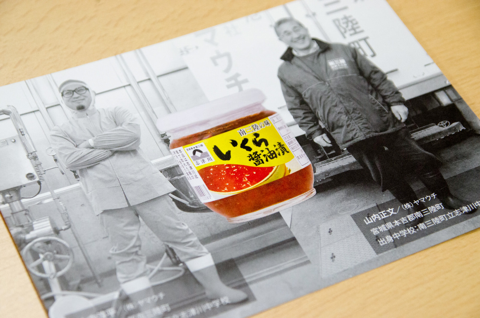 黒白の背景写真に工場作業服を着た男性とトラックの荷台の前に立っている男性が写っており、その中央に「いくら醤油漬」と書かれた瓶詰めのいくら商品がカラーで強調されて配置されているギフトの写真