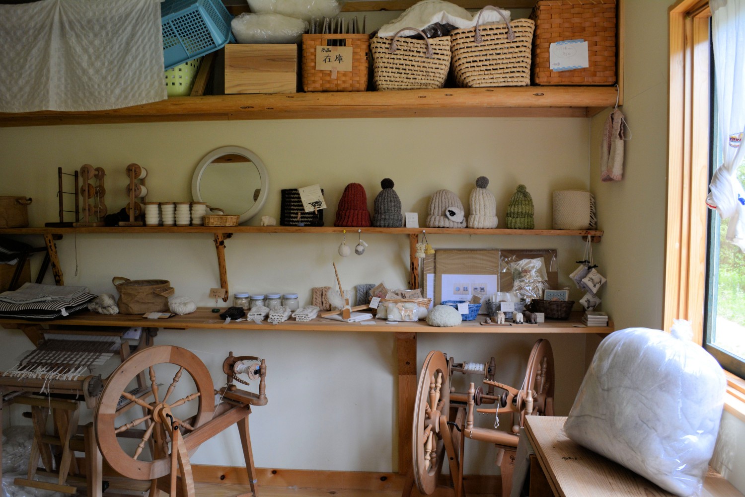 木製の棚に毛糸の帽子や雑貨、手紡ぎの糸、羊毛製品などが並べられ、手前には紡ぎ車も置かれている店内の写真