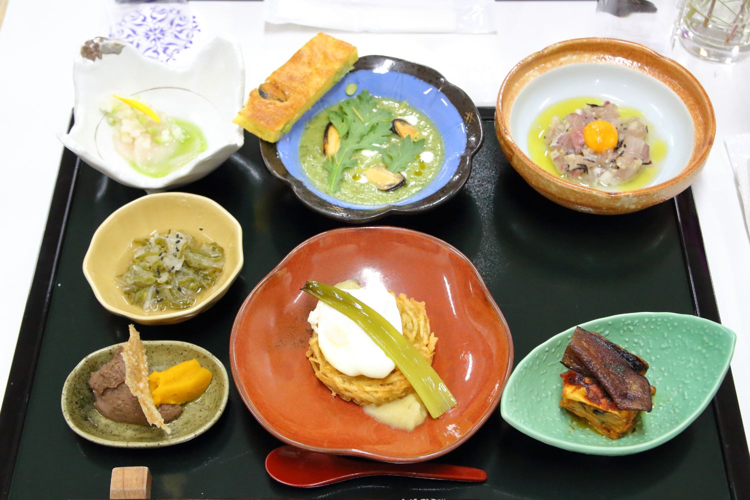 お盆に7枚のお皿が並んで置かれ、それぞれ料理が盛り付けられた写真