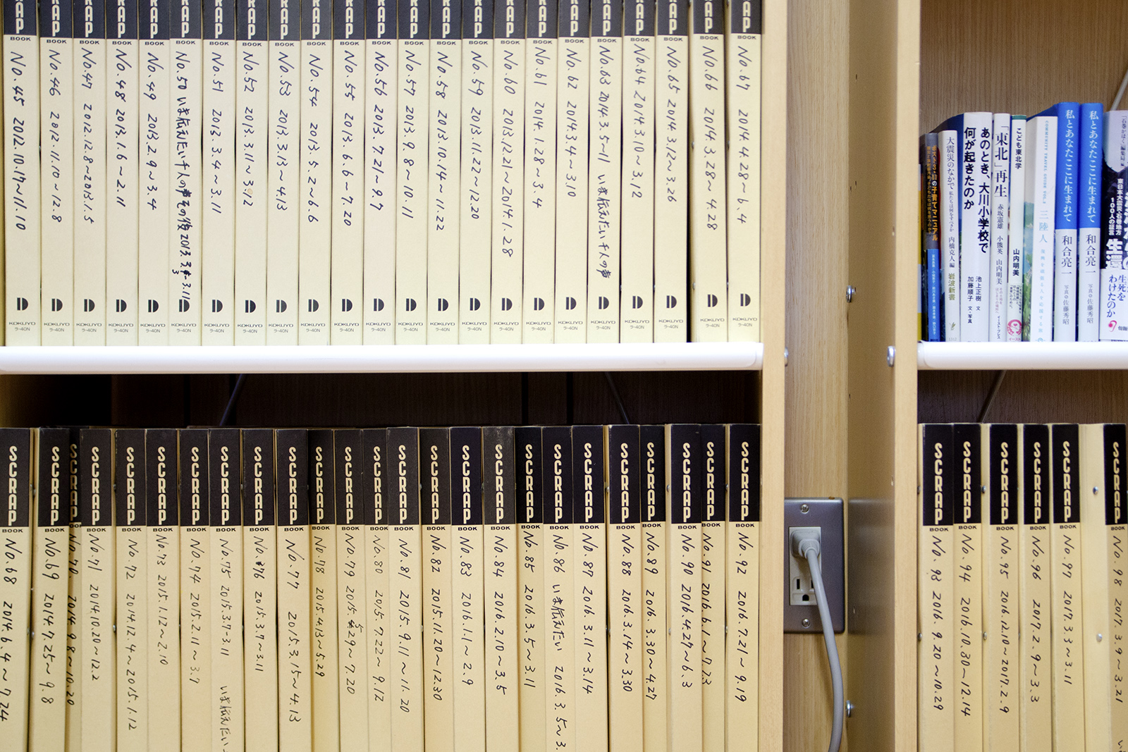 薄い黄色の背表紙のスクラップブックや書籍が並んだ本棚の写真