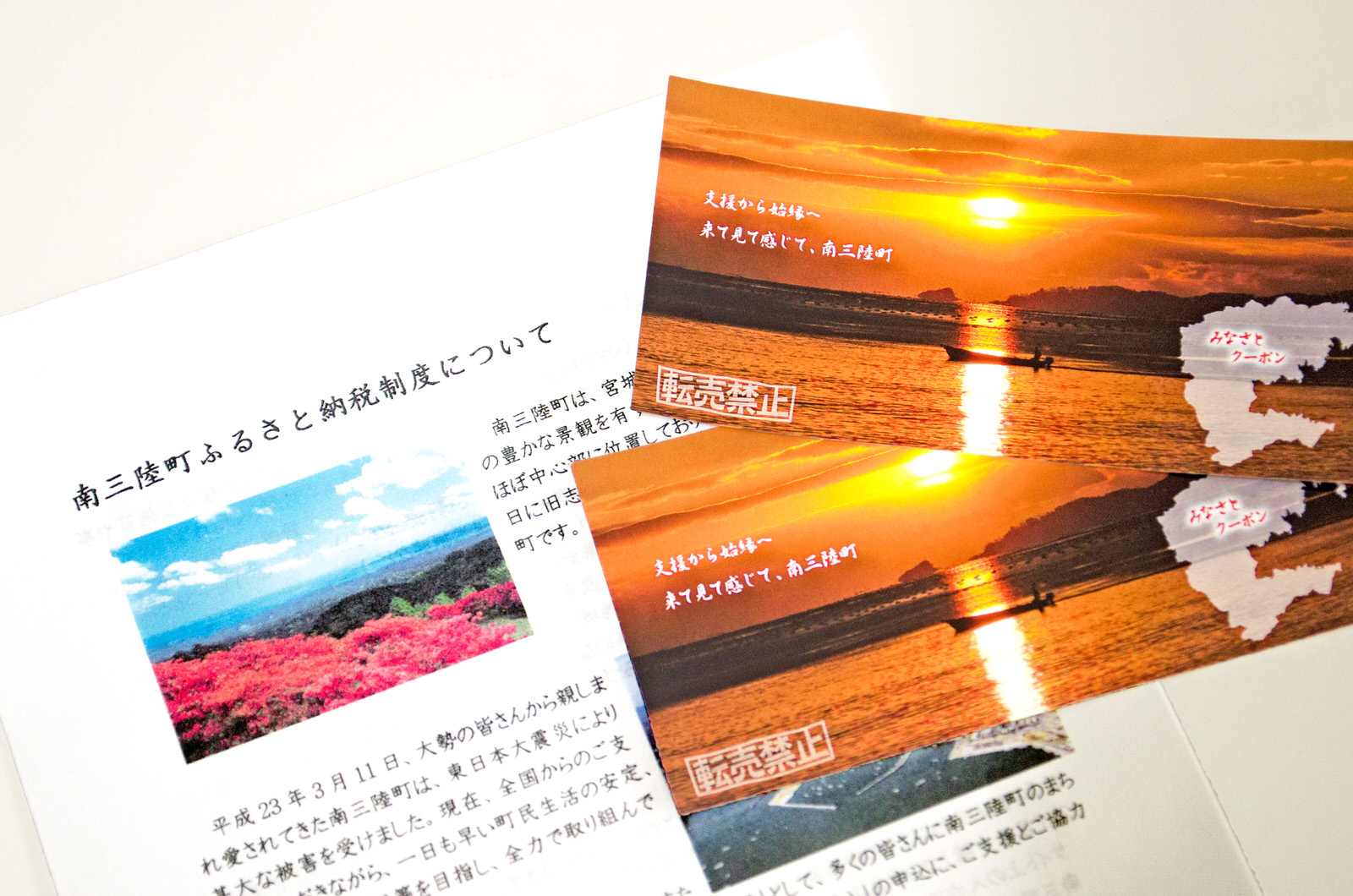 南三陸町ふるさと納税制度の説明文書の上に、夕焼けの海を背景にした2枚の南三陸町のみなさんクーポンが重ねて置かれている写真