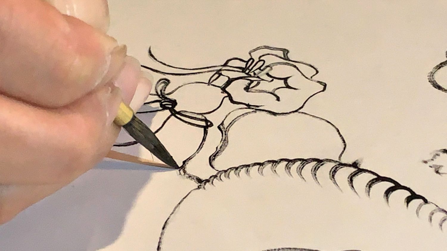 細い墨の線で鋭い爪を持った龍の手と、背のようなギザギザの線を紙に描いている繊細な手元の筆先をアップで撮影した写真